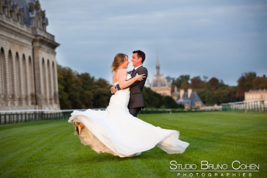 mariés qui dansent sur la piste de l'hippodrome de Chantilly, en arrière-plan, les Grandes Ecuries de Chantilly et le Chateau de Chantilly